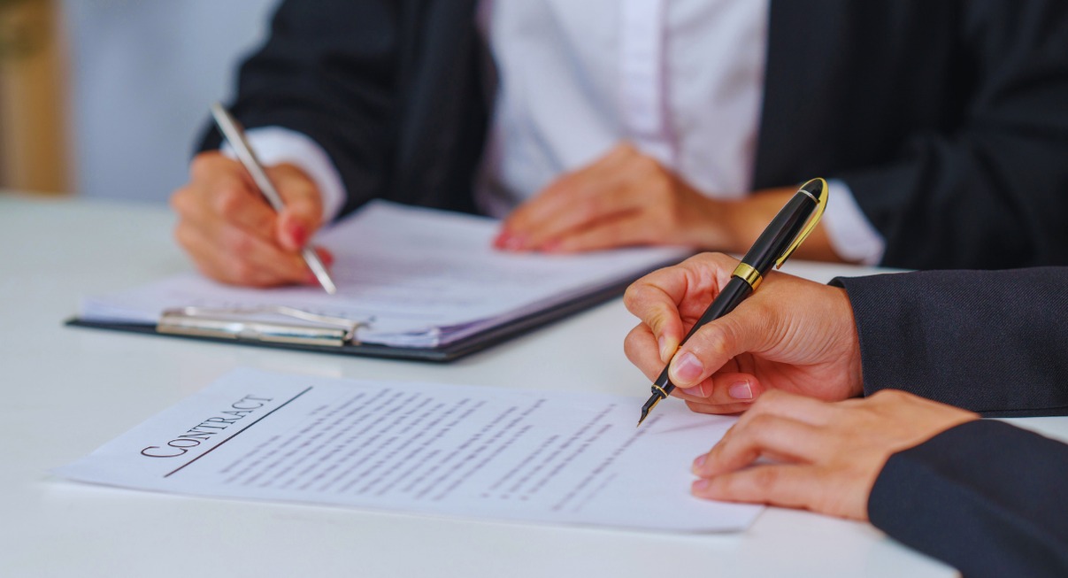 Deux personnes en tenue de bureau signant un contrat papier sur une table blanche